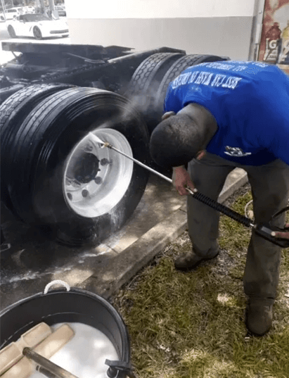 A man is using a hose to clean the tires on a truck.